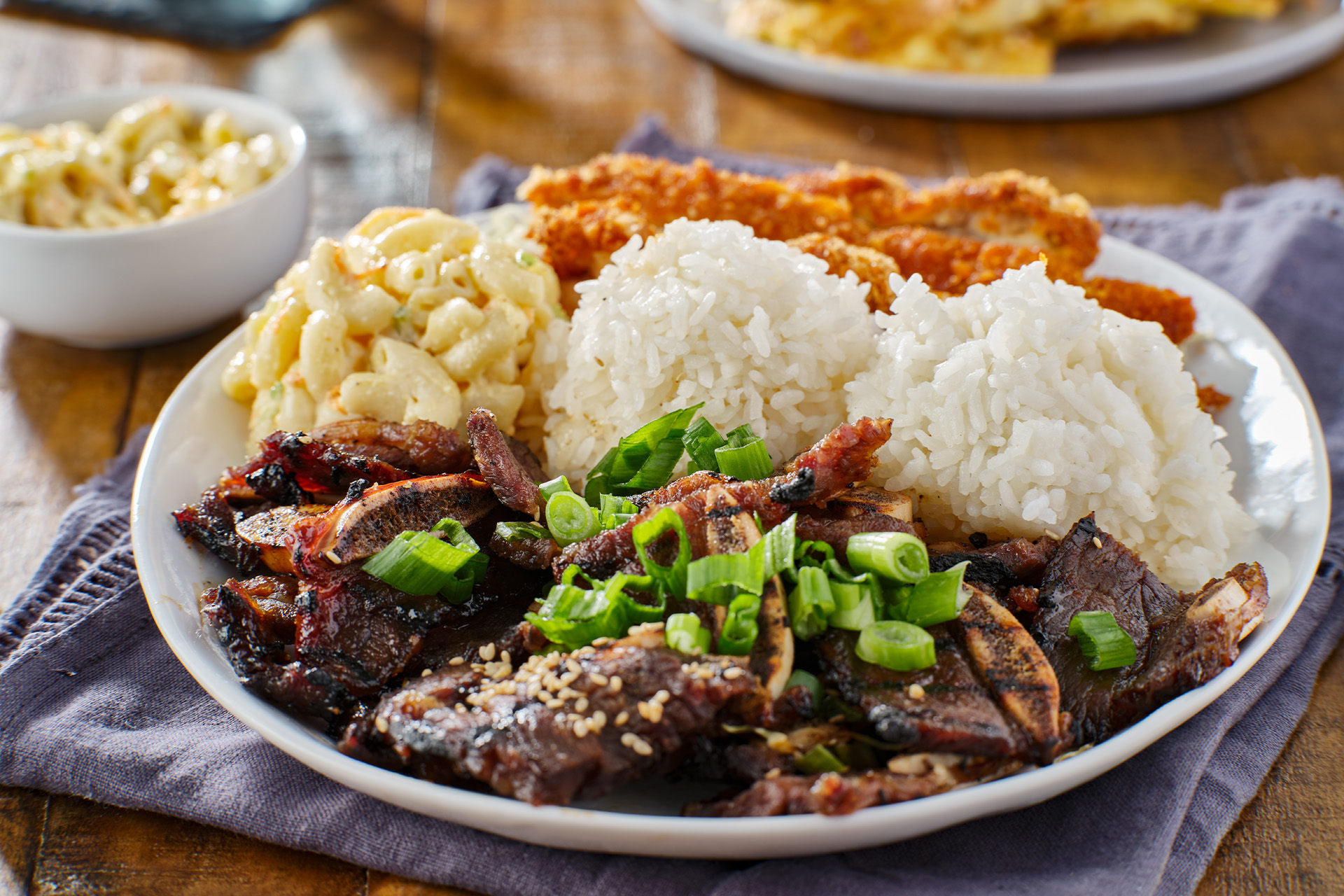 A plate with chicken katsu, korean kalbi beef short ribs, rice, and macaroni salad